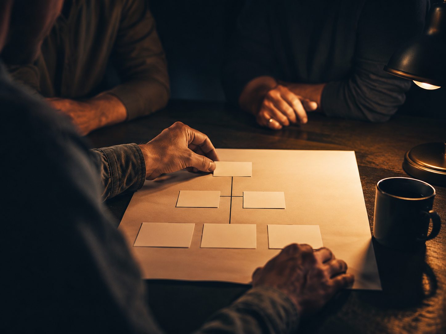 Hands arranging a clear strategy diagram on paper at a dark table